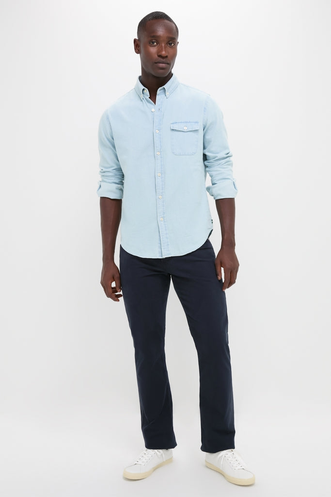 Young man in a classic, light blue washed denim shirt, embodying effortless style with rolled-up sleeves. Paired with navy chinos and white sneakers for a fun, high-end look.