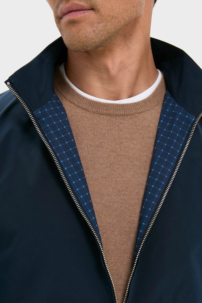 Man in a classic Navy Blue Stanley Jacket with effortless style, featuring a check-patterned lining, layered over a tan sweater and white T-shirt for a high-end, fun look.