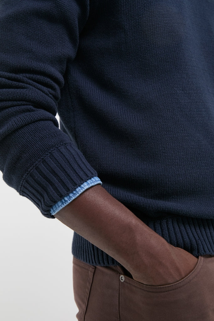 Navy Blue All Season Classic Crewneck exudes effortless style over a light-blue shirt, paired with brown pants, embodying classic, high-end, fun vintage-inspired design.