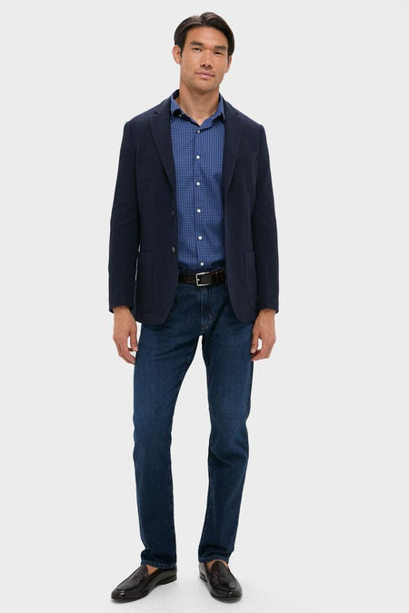 Man in Navy Blue Knit Travel Blazer with a blue checked shirt, dark jeans, and loafers, embodying a classic, effortless, and high-end style for business or travel.