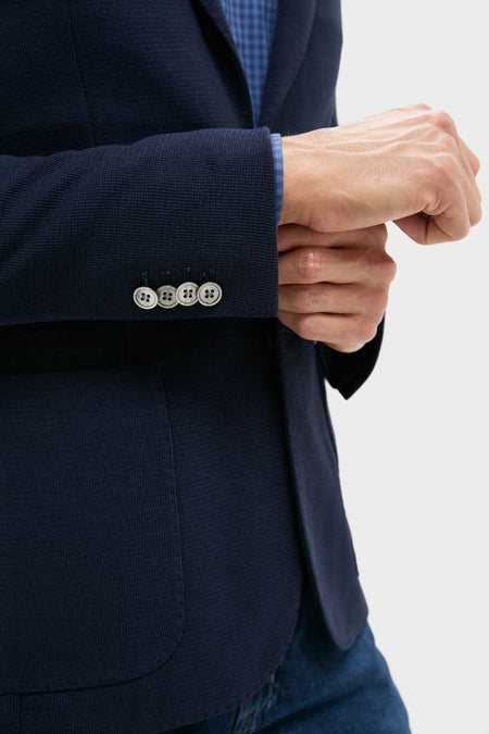 Person adjusting the cuff of a classic Navy Blue Knit Travel Blazer, showcasing effortless style with button detailing, ideal for high-end, fun travel and office wear.