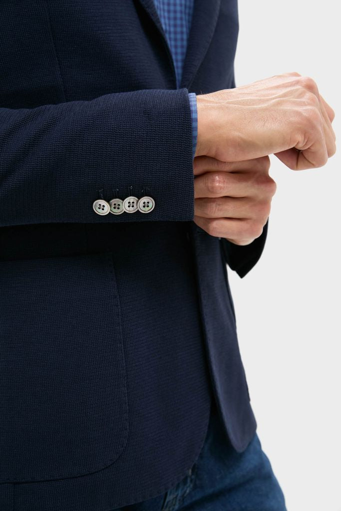 Person adjusting the cuff of a classic Navy Blue Knit Travel Blazer, showcasing effortless style with button detailing, ideal for high-end, fun travel and office wear.