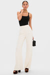 Model wearing Pearl White Crepe Versailles Pant with a high-rise, wide-leg silhouette. Styled with a black tank top, gold necklace, and platform sandals for an effortlessly chic look.