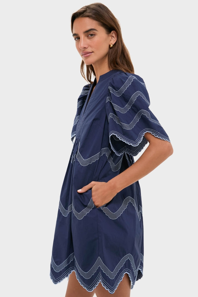Woman models the Navy Embroidered Weston Mini Dress with classic scalloped trims and fluttery sleeves, embodying effortless, high-end style perfect for any fun occasion.