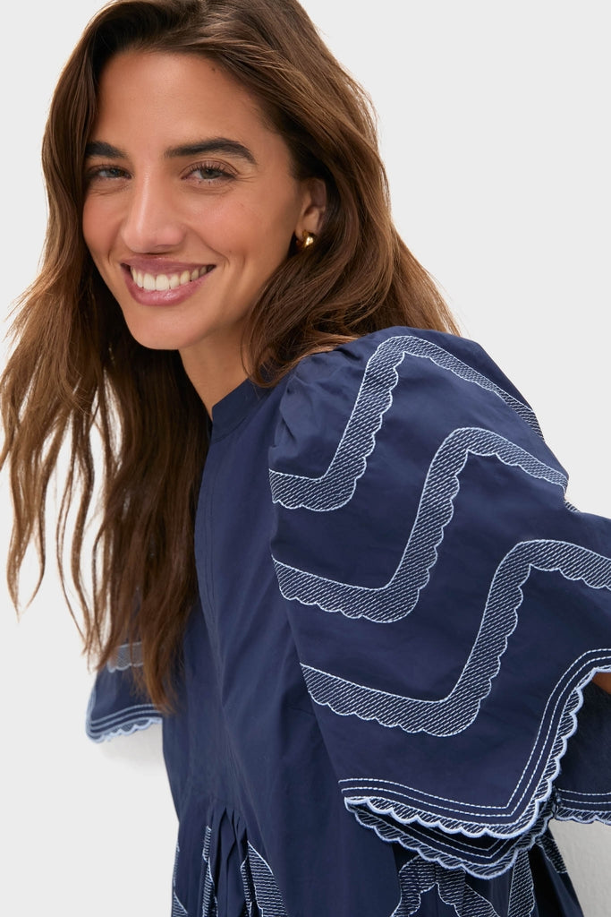 Woman in Navy Embroidered Weston Mini Dress with scalloped trim and gold hoops, embodying classic, effortless style; perfect for fun, high-end occasions.