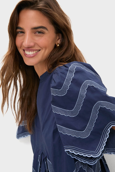 Woman in Navy Embroidered Weston Mini Dress with scalloped trim and gold hoops, embodying classic, effortless style; perfect for fun, high-end occasions.