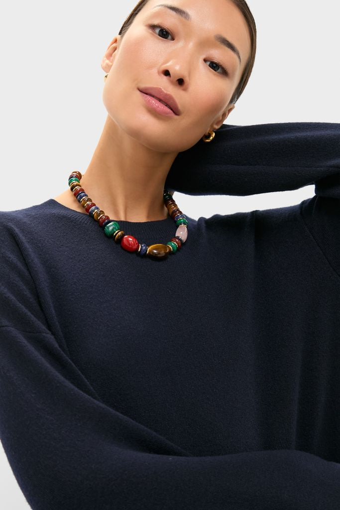 Woman in a classic Navy Vivianne Crewneck Dress with long sleeves and ribbed trim, wearing an effortless, fun, high-end multicolored bead necklace and gold hoop earring.