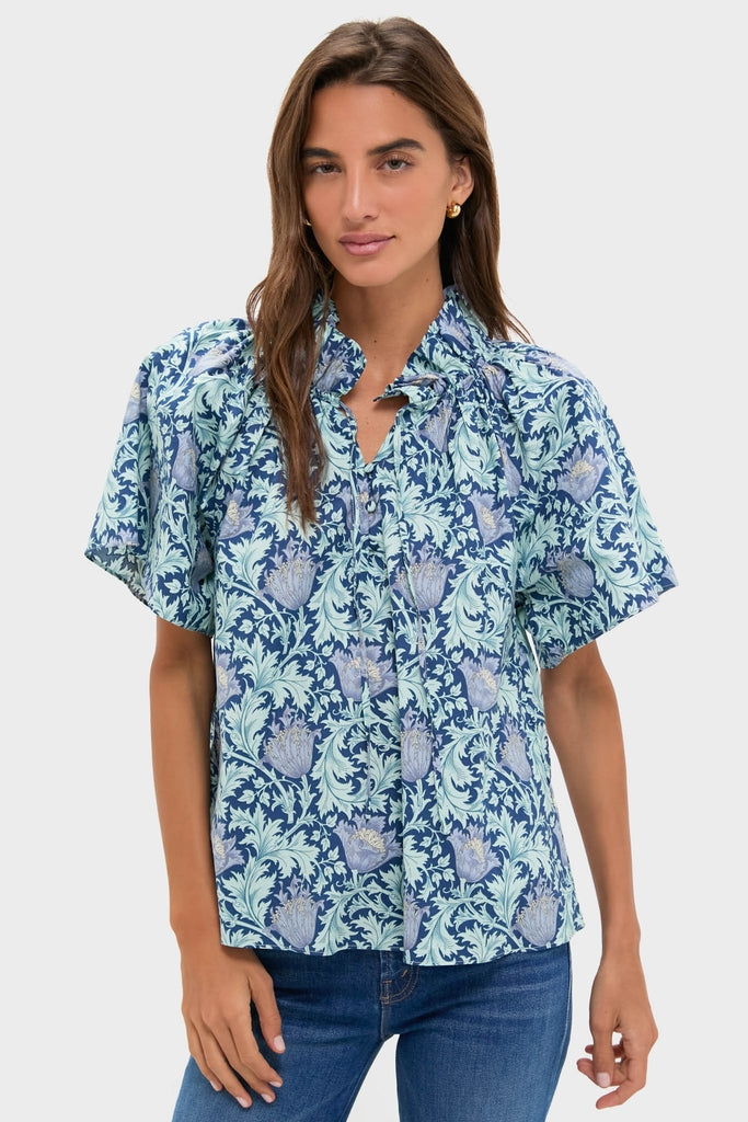 Young woman models the classic, effortlessly fun Multi Blue Leafy Floral Thea Blouse with relaxed fit, ruffle stand collar, and flare sleeves, embodying high-end bohemian charm.