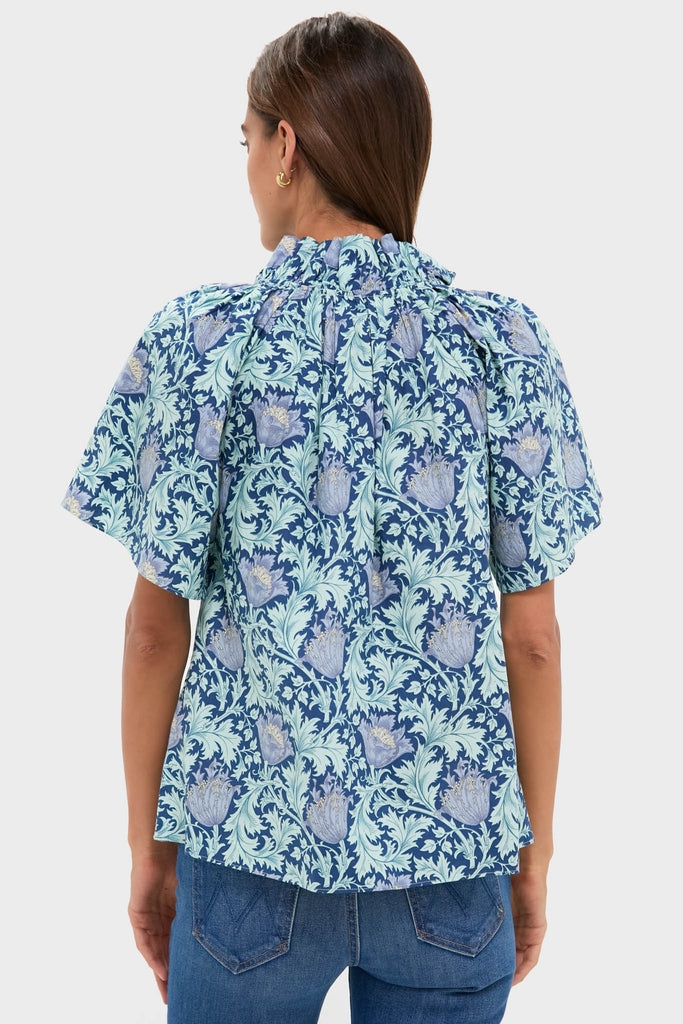 Back view of the Multi Blue Leafy Floral Thea Blouse featuring a classic, effortless design with flutter sleeves and ruffle collar, paired with mid-blue denim for a fun, high-end look.
