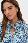 Young woman wearing the Multi Blue Leafy Floral Thea Blouse with a relaxed fit, ruffle collar, and neck-ties, exuding classic, effortless style.