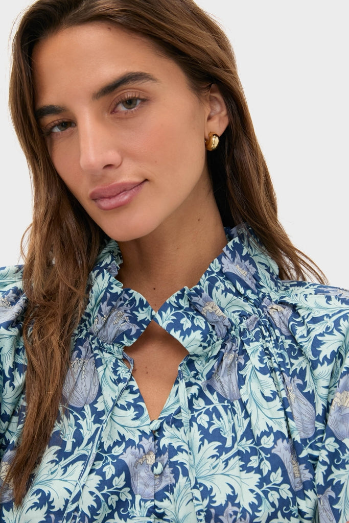 Young woman wearing the Multi Blue Leafy Floral Thea Blouse with a relaxed fit, ruffle collar, and neck-ties, exuding classic, effortless style.