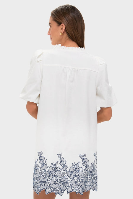 Woman in an effortless, classic White & Navy Embroidery Mimi Mini Dress with puff sleeves and embroidered hem, embodying fun and high-end style.