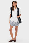 Woman modeling the White & Navy Embroidery Mimi Mini Dress, featuring an effortless classic style with a ruffle collar, puff sleeves, and embroidered hem, paired with chic accessories.