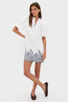 Woman wearing the classic White & Navy Embroidery Mimi Mini Dress with puff sleeves and scalloped hem, embodying effortless fun and high-end style, paired with dark brown flats.