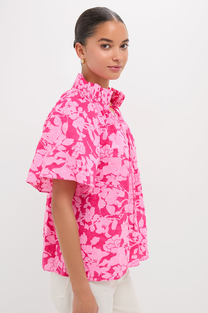 Model in Pink Textured Floral Thea Blouse with ruffle collar and flutter sleeves, embodying classic, effortless style, perfect for a fun, high-end spring look.