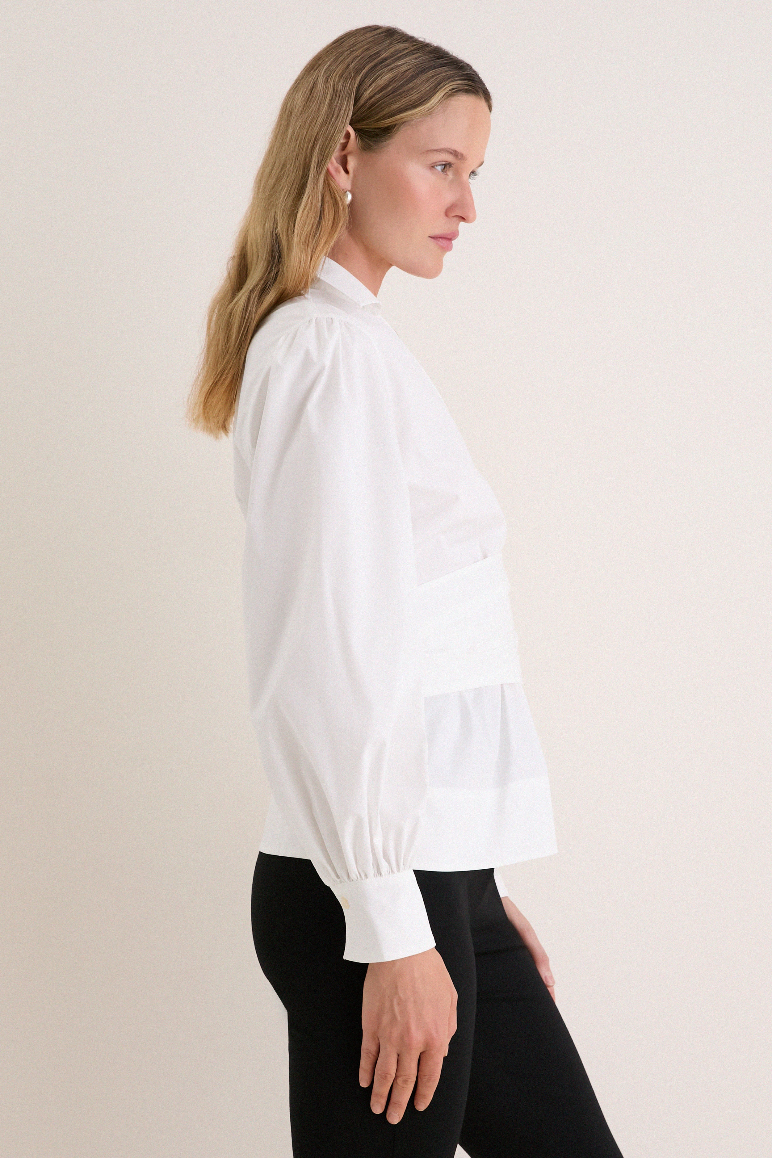 Side-profile of a woman in a classic, effortless White Tie Front Bow Bea Blouse with wrap silhouette, balloon sleeves, showcasing a high-end, fun style.