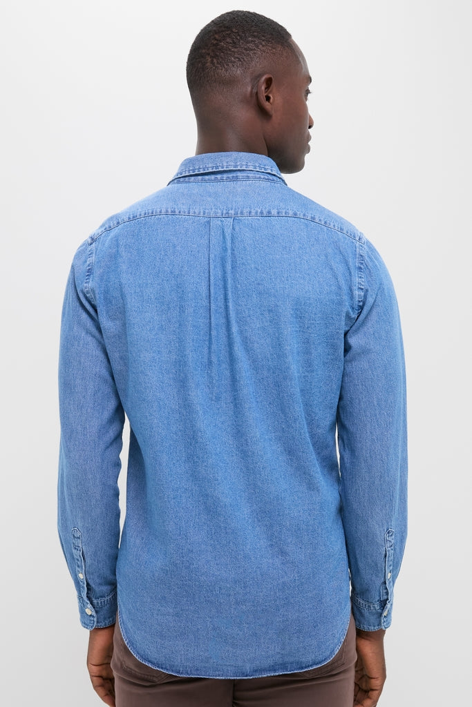 Back view of a classic, effortless Dark Indigo Washed Denim Shirt, showcasing button cuffs and tab collar, worn with brown trousers for a high-end, fun style.