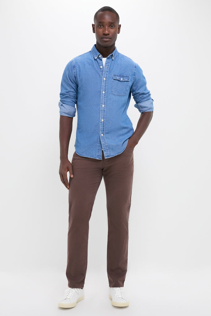 Man models Dark Indigo Washed Denim Shirt; a classic, effortless piece with button cuffs and tab collar, styled casually with brown pants and white sneakers.