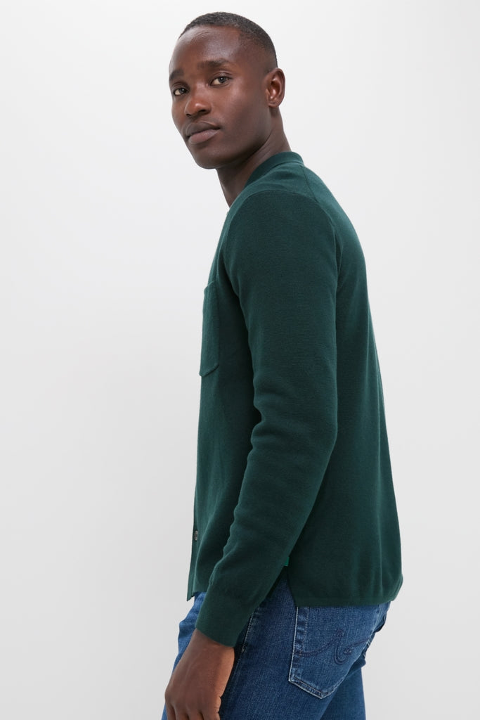 Young man in profile wearing the classic, high-end Forest Green Merino Cardigan, effortlessly styled with medium-wash jeans, showcasing a blend of shirt structure and sweater comfort.