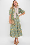 Woman in classic Blue & Green Leafy Floral Cisco Maxi Dress with puff sleeves, taupe clutch, and sandals, embodying effortless, fun, high-end style.