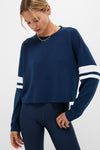 Model wearing Navy Varsity Comfort Stretch Matilda Pullover with white-striped sleeves, paired with high-waisted leggings. Effortless, classic athleisure for a fun, high-end look.