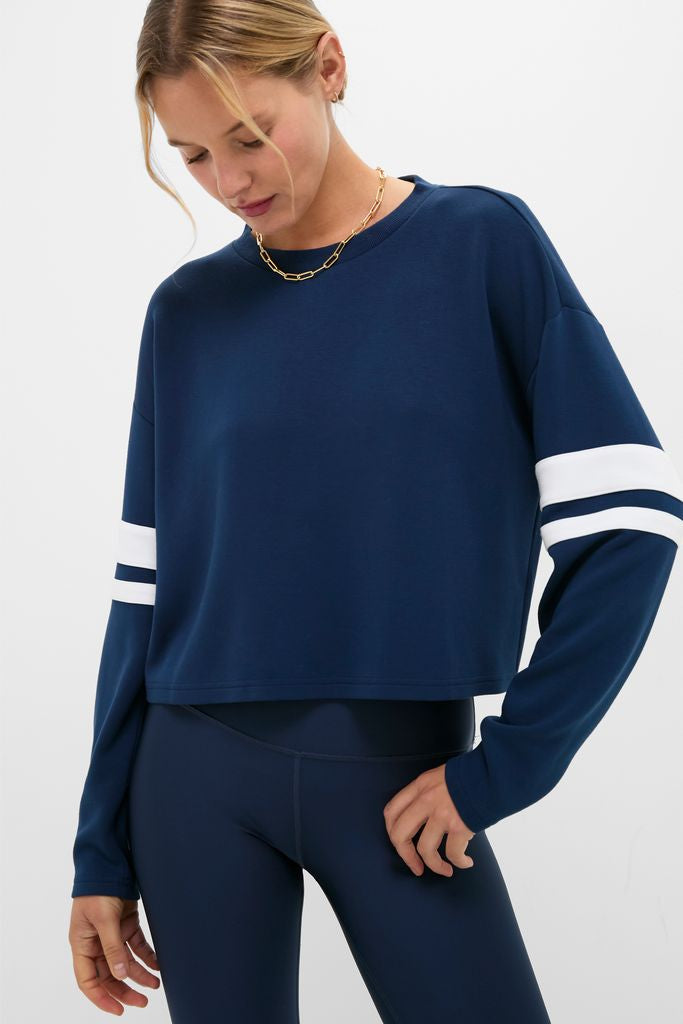 Model wearing Navy Varsity Comfort Stretch Matilda Pullover with white-striped sleeves, paired with high-waisted leggings. Effortless, classic athleisure for a fun, high-end look.