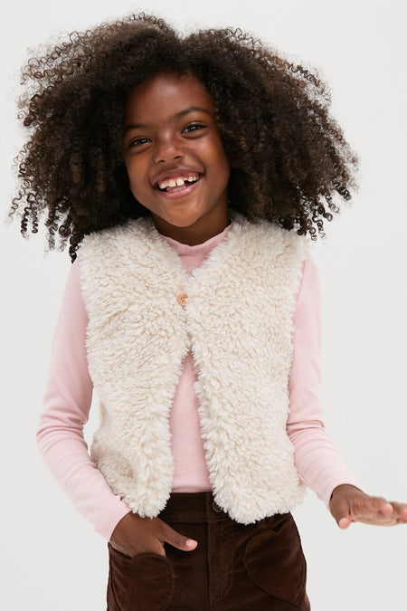 Young girl wearing a classic Cream Teddy Vest over a pink shirt and brown pants, radiating effortless style and fun; perfect for high-end, versatile fashion.