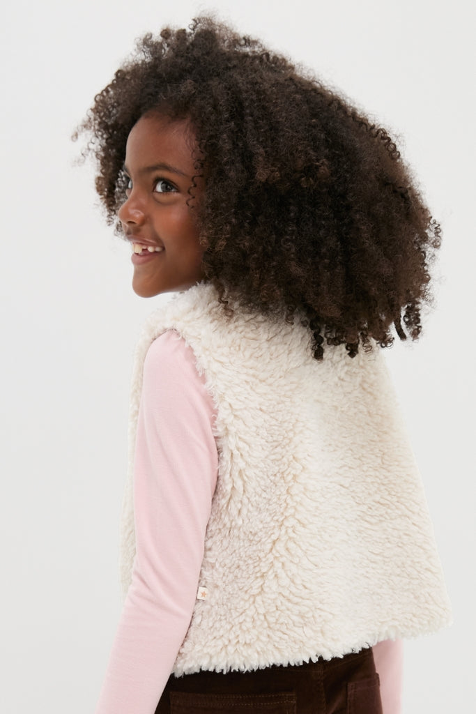 Young girl in a cream Teddy Vest, exuding effortless style with a fun, classic sherpa texture and single button closure, embodying high-end fashion for kids.
