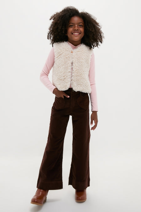 Young girl models a classic, high-end Cream Teddy Vest by BONTON, layered over a pink top, embodying effortless, fun style with corduroy pants and boots.