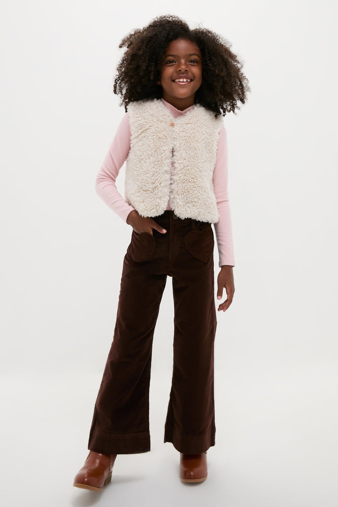 Young girl models a classic, high-end Cream Teddy Vest by BONTON, layered over a pink top, embodying effortless, fun style with corduroy pants and boots.