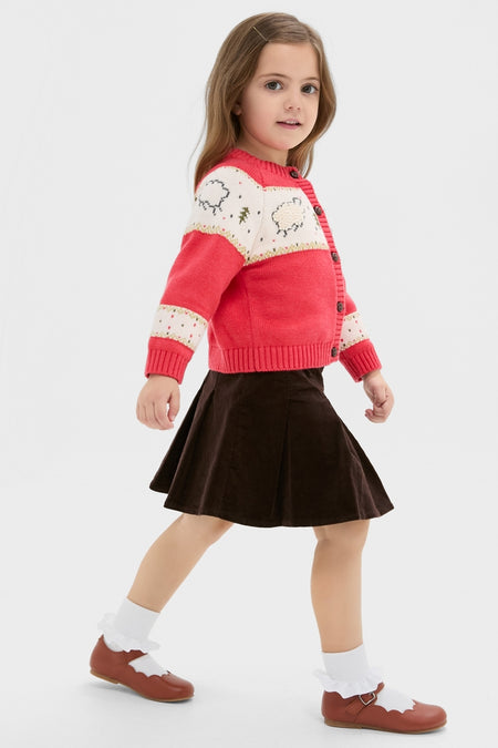 Young girl in a classic, effortless Red Lamb Sweater with playful sheep motifs, button front, and ribbed hems, styled with a brown skirt and Mary Jane shoes.