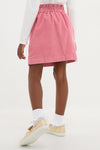 Child wearing classic Pink Douchka Skirt with heart-shaped pockets, paired with a white top and gold sneakers. Effortless style for fun, high-end fashion.