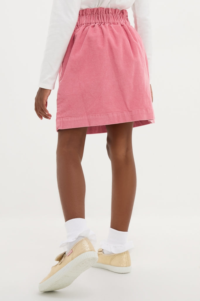 Child wearing classic Pink Douchka Skirt with heart-shaped pockets, paired with a white top and gold sneakers. Effortless style for fun, high-end fashion.