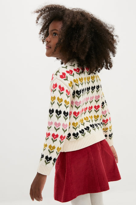 Young girl in a classic Multi Floral Sweater with tulip patterns, embodying effortless, high-end style, paired with a red corduroy skirt, perfect for fun explorations.