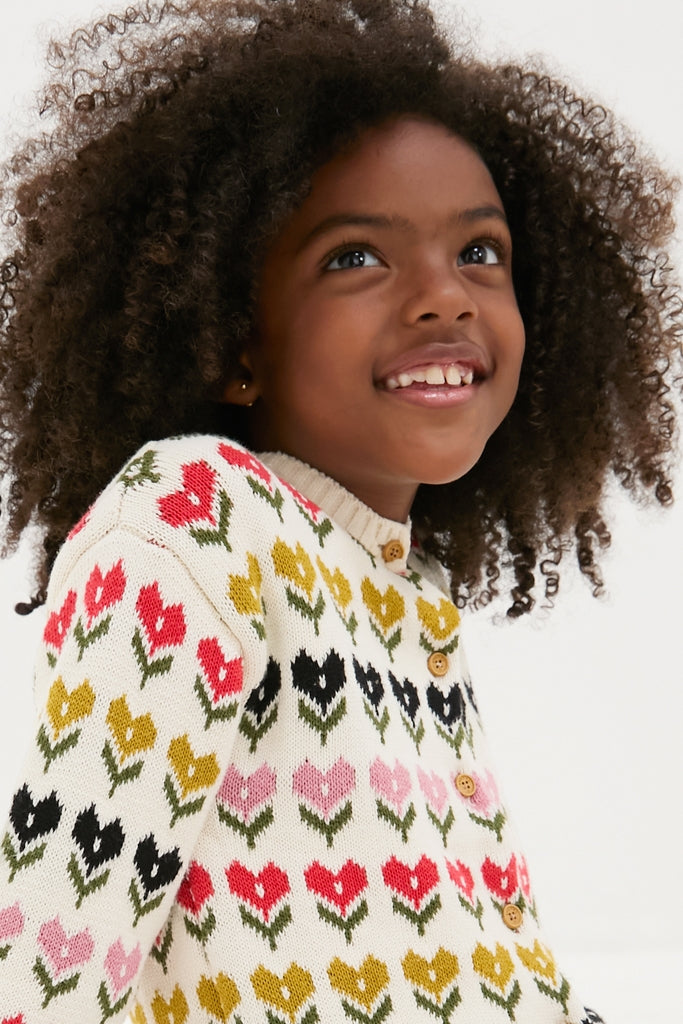 Child smiling in a classic, high-end Multi Floral Sweater, showcasing effortless style with fun tulip motifs and wooden buttons, perfect for little explorers.