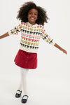 Young girl in a Multi Floral Sweater, radiating classic, effortless style, paired with a red skirt and Mary Jane shoes, embodying fun, high-end fashion.