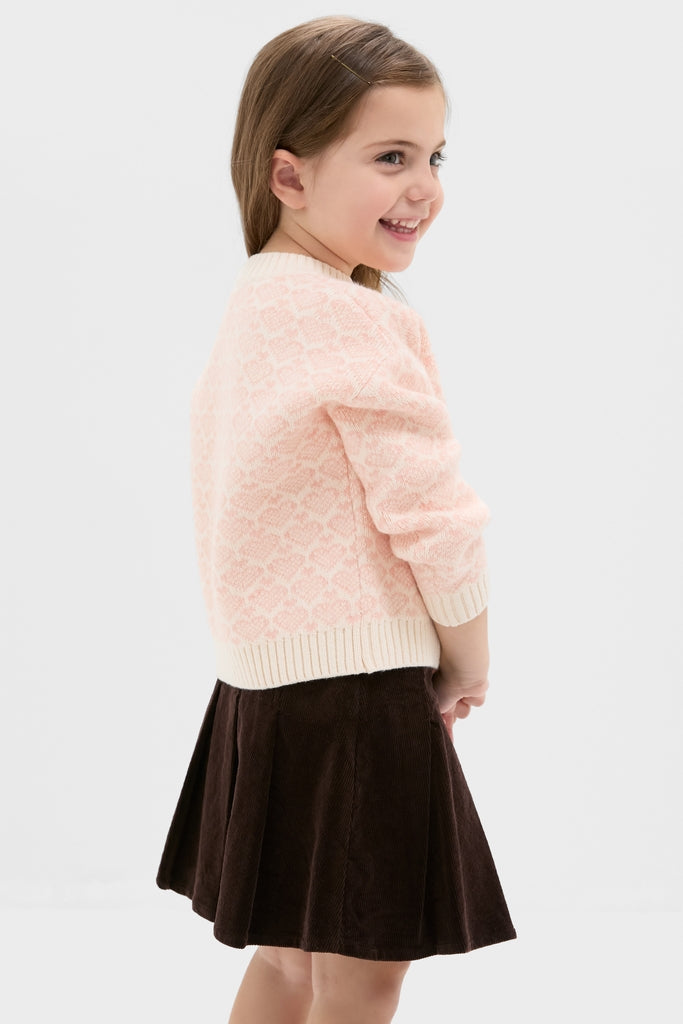 Young girl in classic Light Pink Heart Sweater, exuding effortless style and fun, paired with a dark brown corduroy skirt, embodying high-end winter fashion.