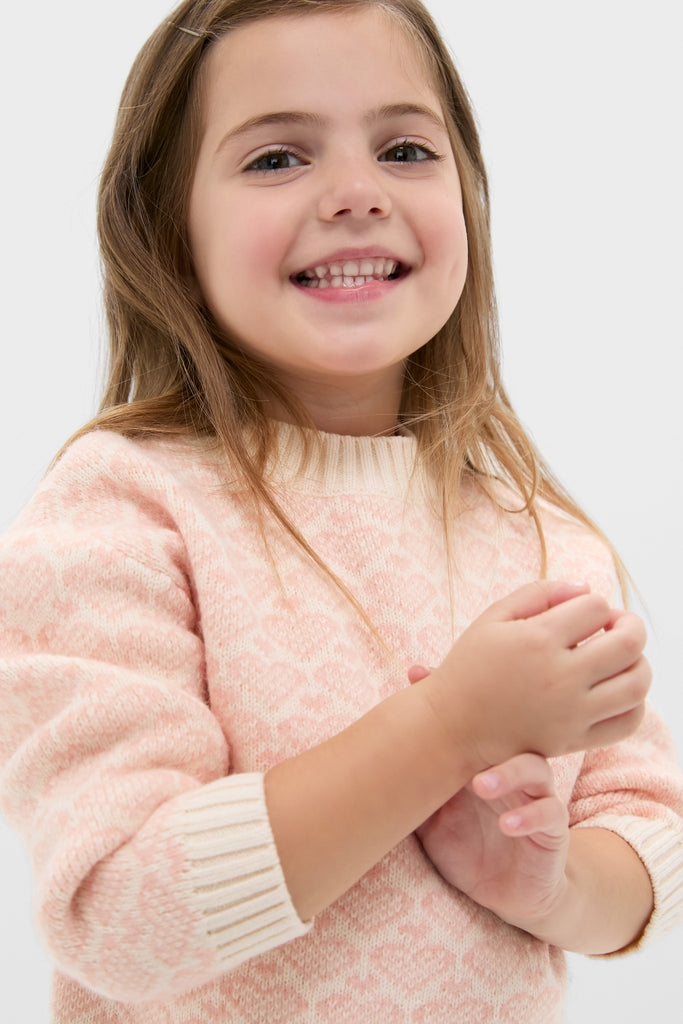 Young girl in a classic, pale pink heart sweater, embodying effortless style and fun. The high-end knitwear, perfect for winter, showcases BONTON's Parisian touch.