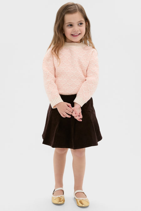 Young girl wearing a classic Light Pink Heart Sweater with ribbed knit finishes, paired effortlessly with a dark brown A-line skirt and gold Mary Jane shoes, exuding fun, high-end style.