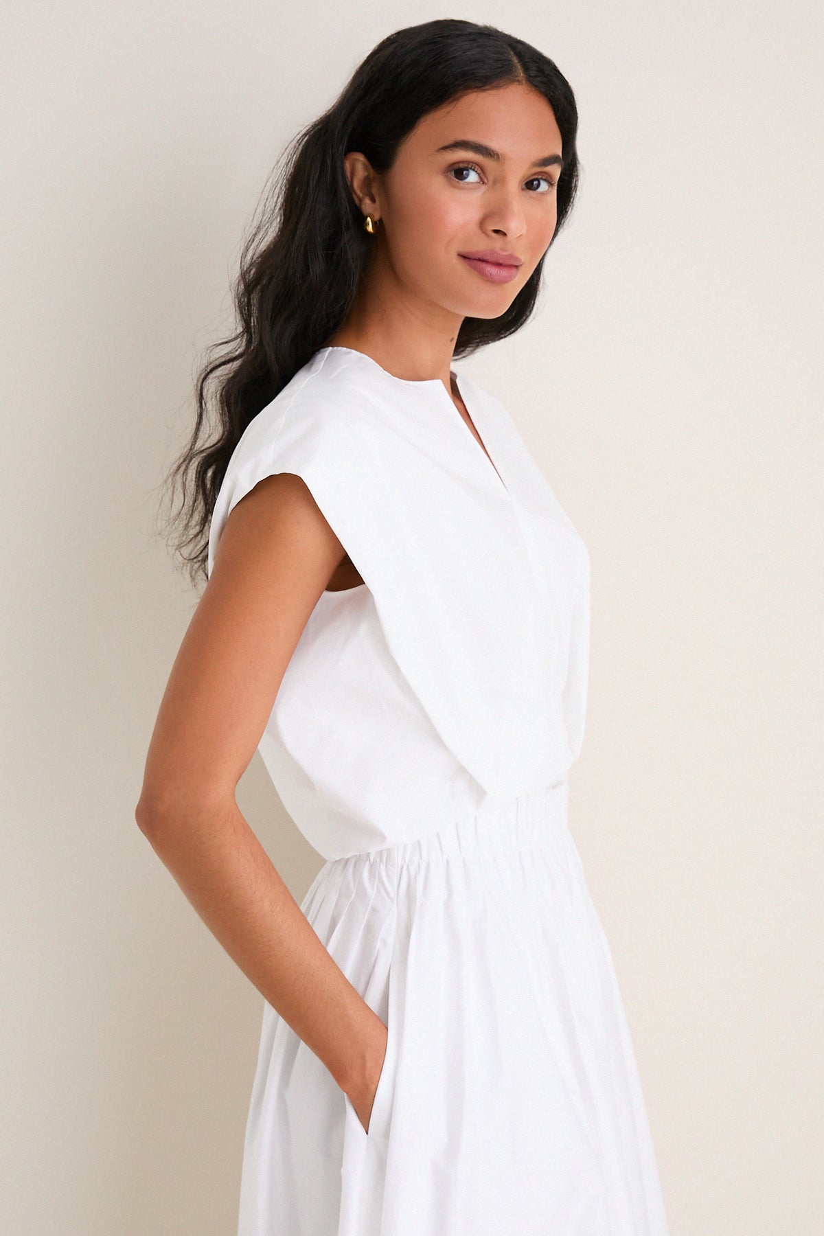 Young woman models the White Wrenli Shortsleeve Pleated Top, showcasing its classic, effortless style with cap sleeves and hem pleats, embodying high-end, fun fashion.