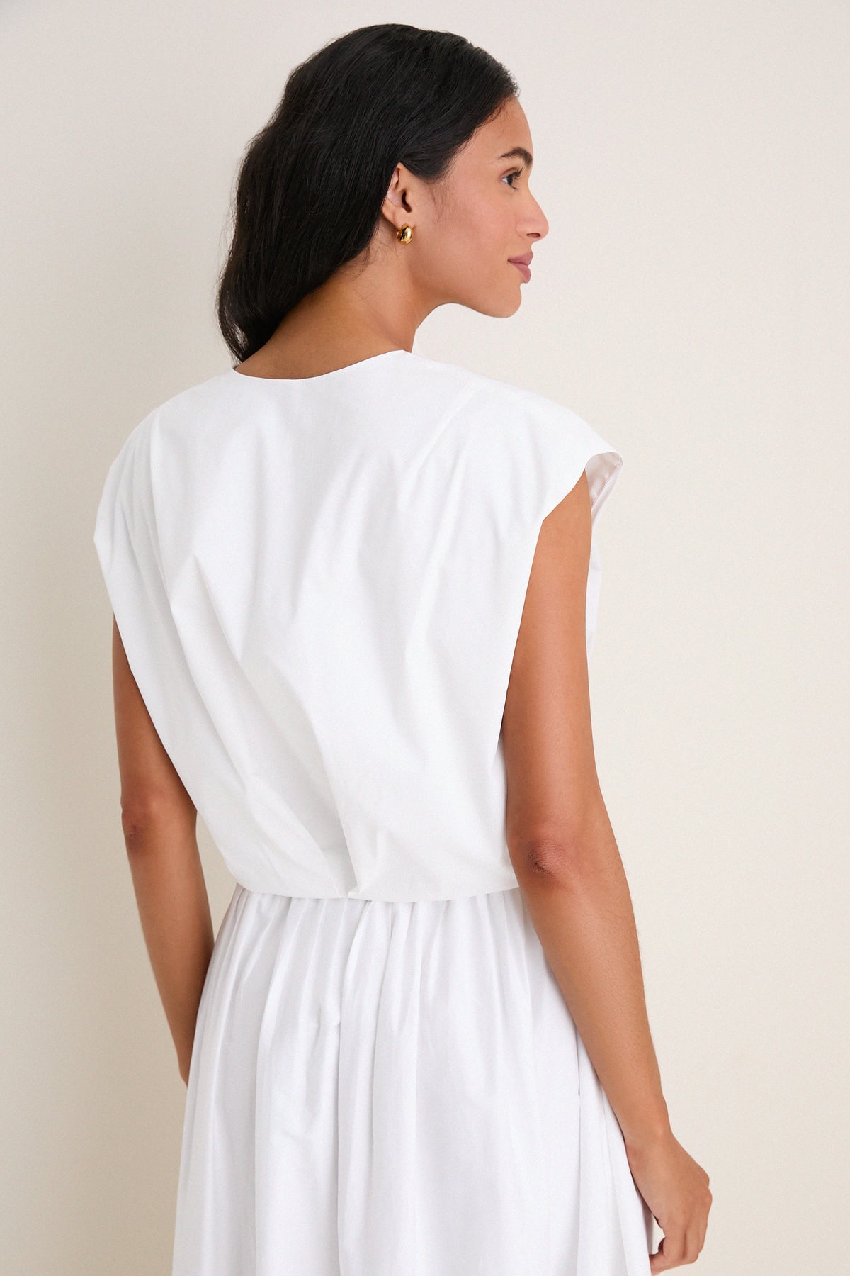 Woman in profile wearing the White Wrenli Shortsleeve Pleated Top with cap sleeves and pleated hem, embodying a classic, effortless, high-end style.