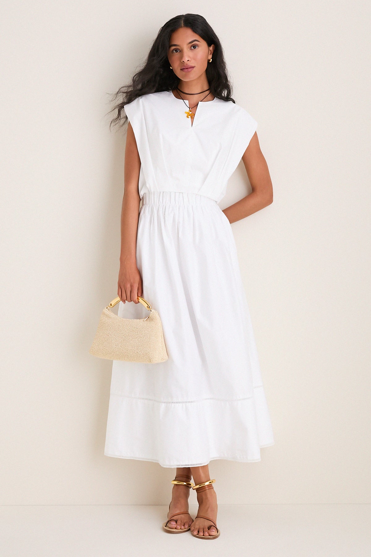 Woman models the classic White Wrenli Shortsleeve Pleated Top with cap sleeves and a split v-neck, exuding effortless, high-end style paired with a chic handbag and sandals.