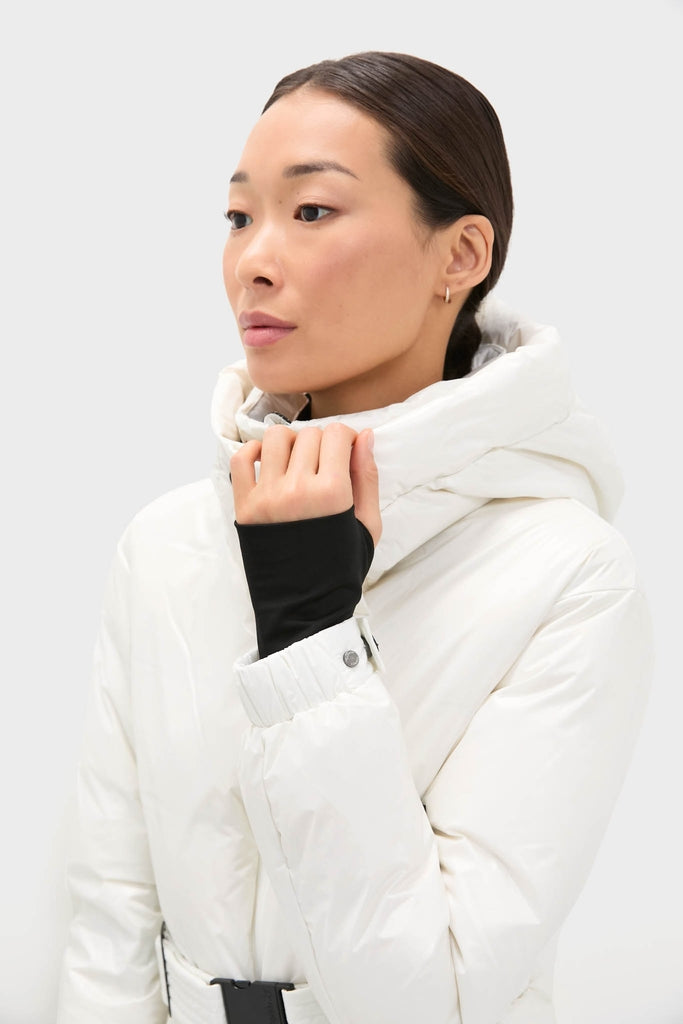 Woman models the Snow White Candice Ski Parka, featuring a glossy, belted silhouette and high collar, effortlessly blending classic elegance with high-end, fun, and functional ski-ready features.