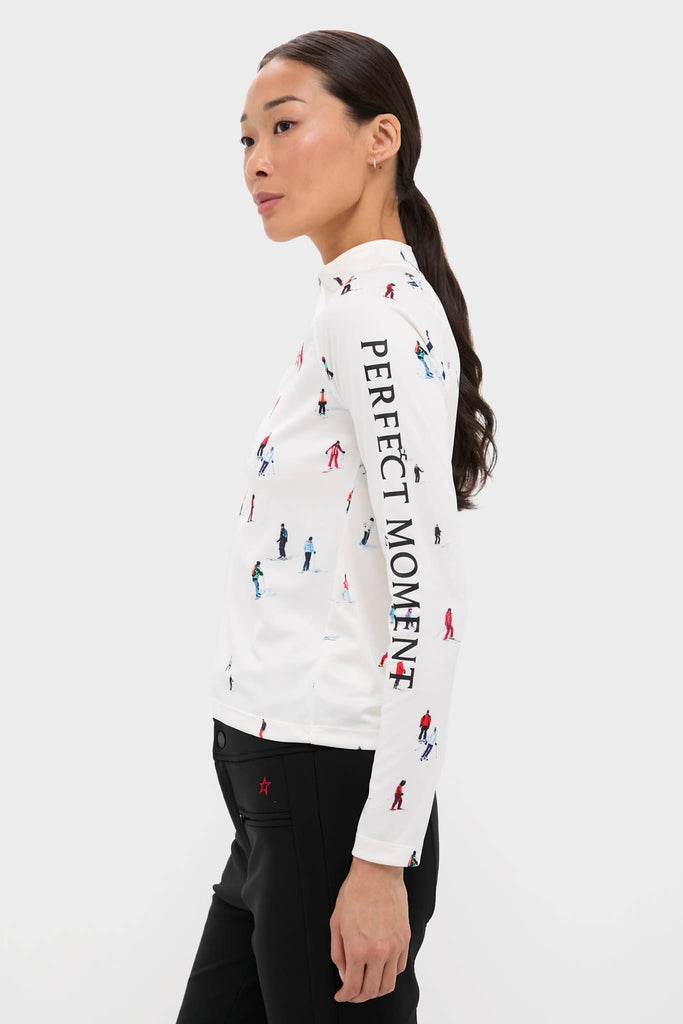 Woman in profile wearing the classic, effortless Dede Ski Print 1/4 Zip Base Layer Top, featuring colorful skier figures and PERFECT MOMENT text, paired with high-end black pants.