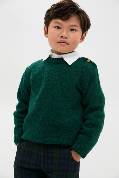 Young boy in a classic, dark-green Forest Green Bromo Merino Boy Jumper with button detail, layered over a white shirt; an effortless, high-end preppy look.