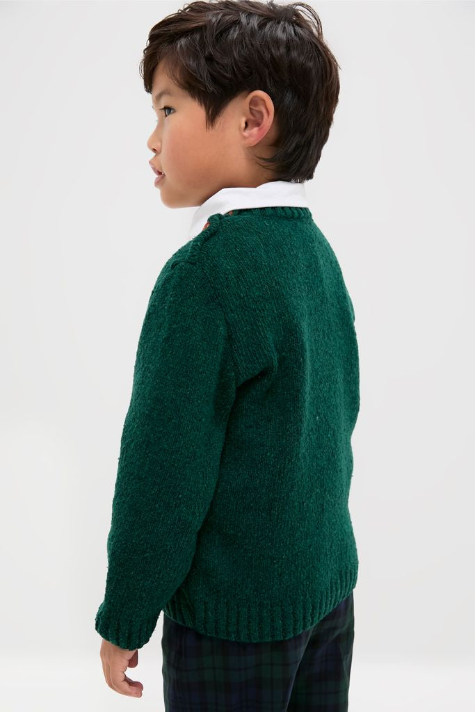 Young boy in profile wearing the Forest Green Bromo Merino Boy Jumper, a classic, high-end sweater with effortless style, featuring buttons and ribbed finishes for a fun, timeless look.