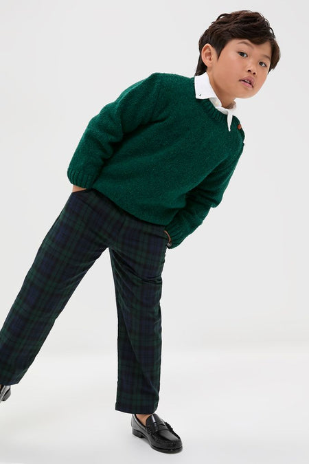 Young boy modeling the Forest Green Bromo Merino Boy Jumper, a classic, high-end sweater with raglan sleeves and shoulder buttons, paired with plaid trousers and loafers.