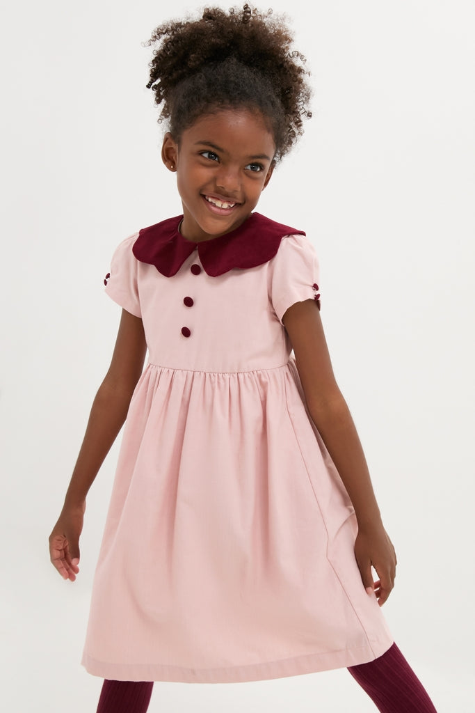 Child in a classic Pink Julieta Girl Dress with puffed sleeves and burgundy accents, embodying effortless, high-end style. Perfect for fun, picture-perfect moments.