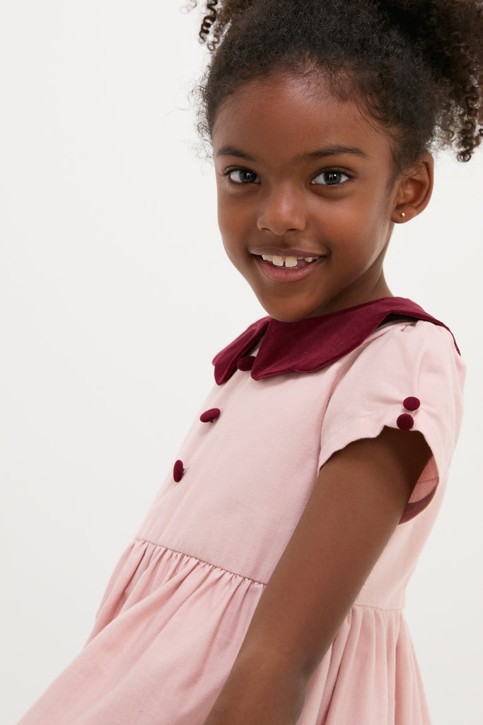 Young girl smiles in a classic, high-end Pink Julieta Girl Dress with an effortless fit, featuring a burgundy velvet scalloped collar and nostalgic button details.