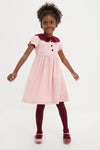 Young girl in classic, high-end Pink Julieta Girl Dress with a velvet burgundy collar, effortlessly playful in ribbed tights and Mary Jane shoes, embodying fun timeless style.